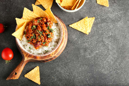 Bowl with tasty chili con carne, rice, nachos and tomatoes on dark backgroundの写真素材