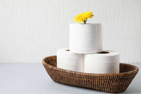 Basket with rolls of toilet paper and flower on light backgroundの写真素材