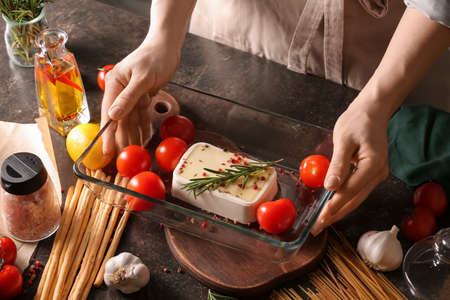 Woman and baking dish with feta cheese on table in kitchenの写真素材