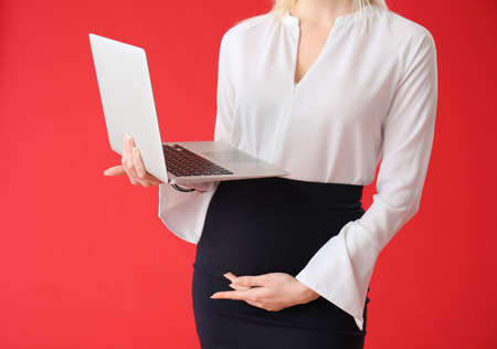 Pregnant young woman with laptop on color backgroundの写真素材