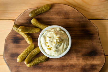 Bowl with tasty tartare sauce and pickled cucumbers on wooden background