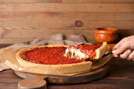 Woman taking a piece of tasty Chicago-style pizza on wooden backgroundの写真素材