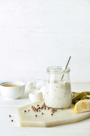 Glass jar with tasty tartare sauce and ingredients on light backgroundの写真素材