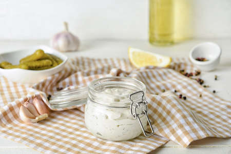 Glass jar with tasty tartare sauce, lemon and pickled cucumbers on light backgroundの写真素材