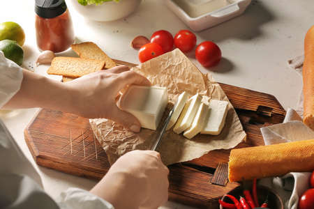 Woman cutting feta cheese on table in kitchenの写真素材