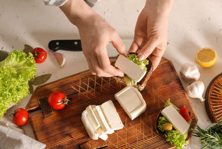 Woman making sandwich with feta cheese on table in kitchenの写真素材