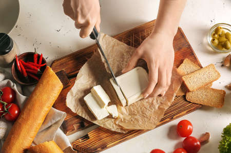 Woman cutting feta cheese on table in kitchenの写真素材
