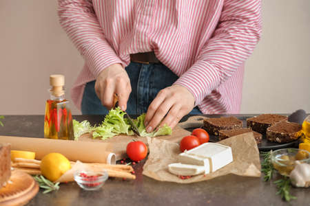 Woman cutting lettuce salad on table in kitchenの写真素材