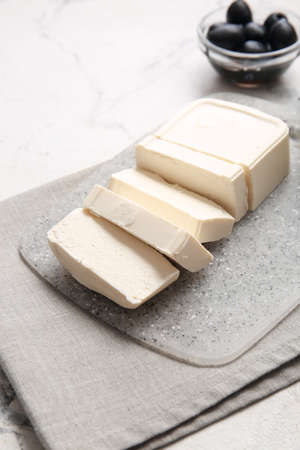 Board with feta cheese and olives on light background