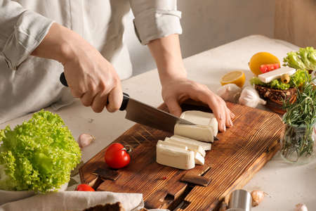 Woman cutting feta cheese on table in kitchen