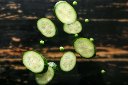 Flying cucumber slices and peas on dark wooden backgroundの写真素材