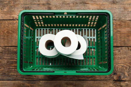 Shopping basket with rolls of toilet paper on wooden backgroundの写真素材