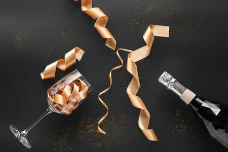 Glass with golden ribbons and bottle of champagne on dark backgroundの写真素材