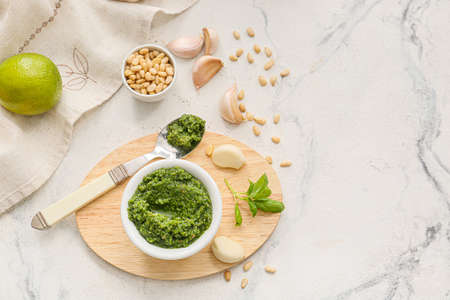 Wooden board with bowl of fresh pesto sauce and ingredients on tableの写真素材