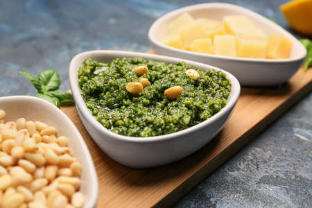 Wooden board with bowl of fresh pesto sauce and ingredients on tableの写真素材