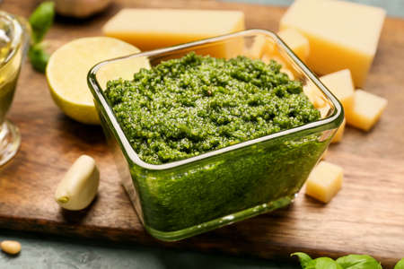 Wooden board with bowl of fresh pesto sauce and ingredients on tableの写真素材