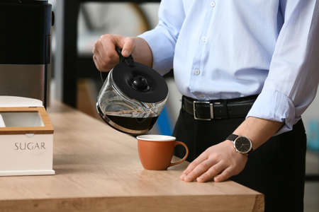 Young man pouring coffee into cup in office