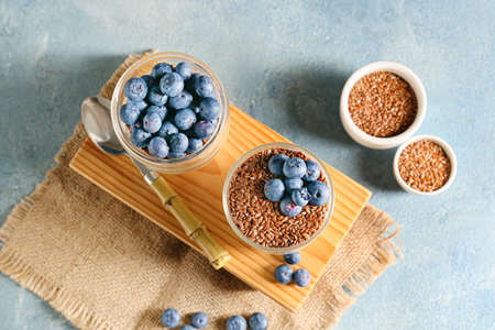 Glasses of sweet yogurt, flax seeds and blueberries on color backgroundの写真素材
