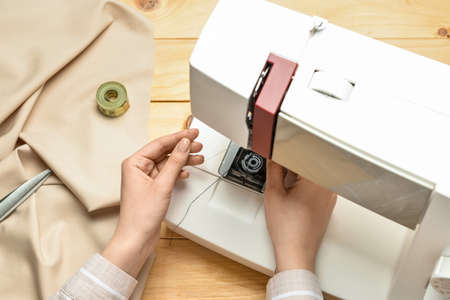 Woman using sewing machine on wooden background