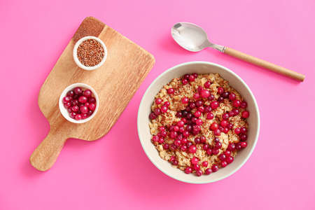 Bowl with tasty oatmeal, flax seeds and cranberries on color backgroundの写真素材