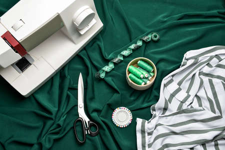 Sewing machine with tailor's supplies and clothes on fabric background