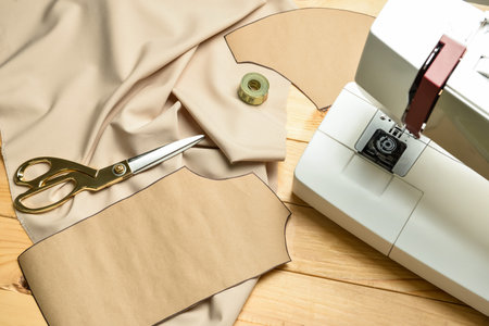 Sewing machine with fabric and tailor's supplies on wooden background