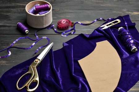 Tailor's supplies with fabric on dark wooden background