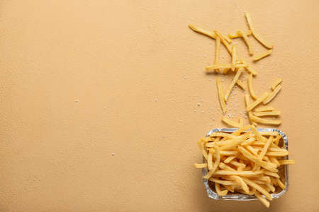 Foil container with tasty french fries on color background