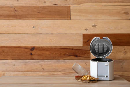 Modern deep fryer and tasty potato on table near wooden wallの写真素材