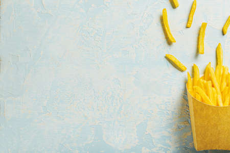 Paper bag with tasty french fries on color background