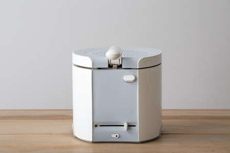 Modern deep fryer on table near light wall