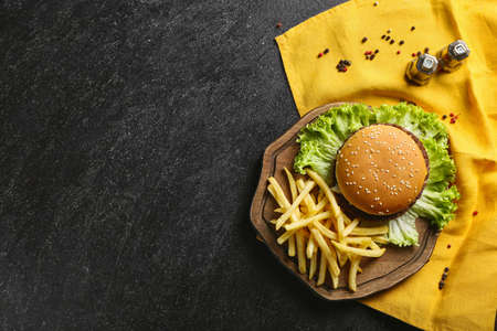 Board with tasty french fries, burger and sauce on dark background