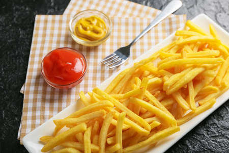 Plate with tasty french fries and sauces on dark background, closeup