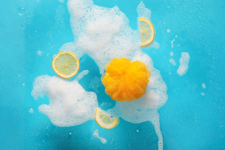 Loofah, lemon and foam on color background with water drops