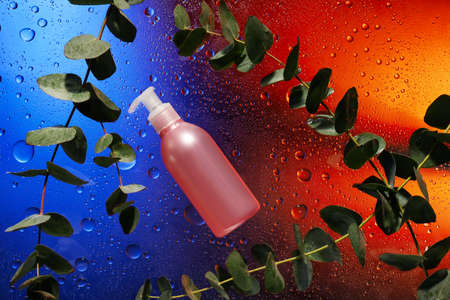 Bottle of cosmetic product and eucalyptus on color background with water dropsの写真素材
