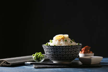 Bowl with tasty rice, green peas and egg on dark background