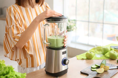 Young woman preparing healthy green smoothie in the kitchenの写真素材
