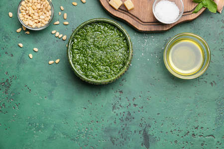 Bowl of tasty pesto sauce and ingredients on green backgroundの写真素材
