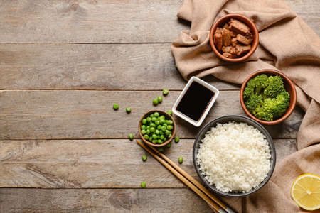 Bowls with tasty rice, meat and vegetables on wooden background