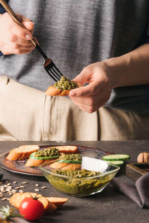 Woman making tasty toasts with pesto sauce on table, closeup
