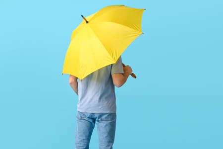 Handsome young man with umbrella on color background
