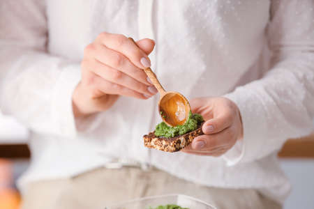Woman making tasty toast with pesto sauce, closeup