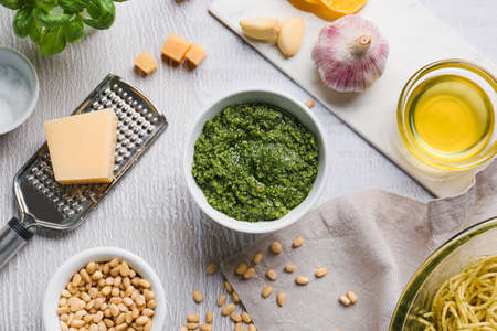 Bowl of pesto sauce and ingredients on light background