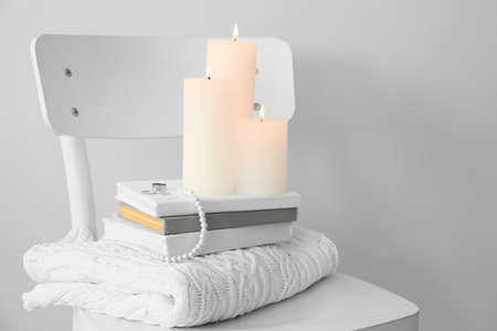 Chair with sweater, books and burning candles on light backgroundの写真素材