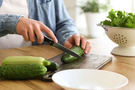 Young man cutting cucumber in kitchen, closeupの写真素材