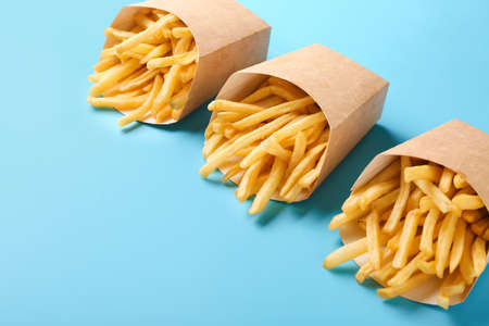 Paper boxes with tasty french fries on color background