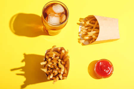 Paper boxes with tasty french fries, tomato sauce and glass of beverage on color backgroundの写真素材