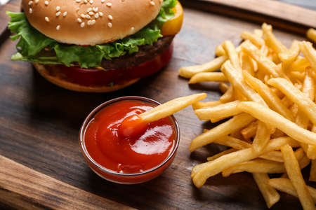 Tasty french fries, tomato sauce and burger on wooden board