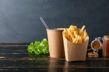 Paper box with tasty french fries and cup of beverage on dark wooden backgroundの写真素材