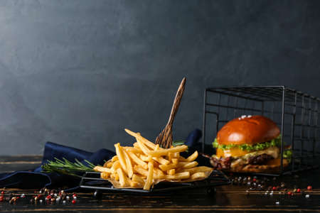 Tasty french fries and burger on dark wooden background